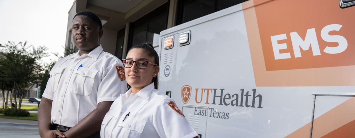 A man and a woman standing next to a UT Health labeled ambulance